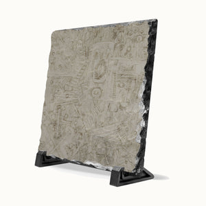 A square stone tile with a textured, etched surface and rough dark edges, displayed on a black metal stand against a white background.