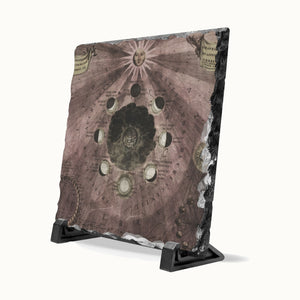 A square slate tile with a rustic, aged parchment design featuring celestial maps, moon phases, and an astrological sun face, displayed on a black stand against a white background.