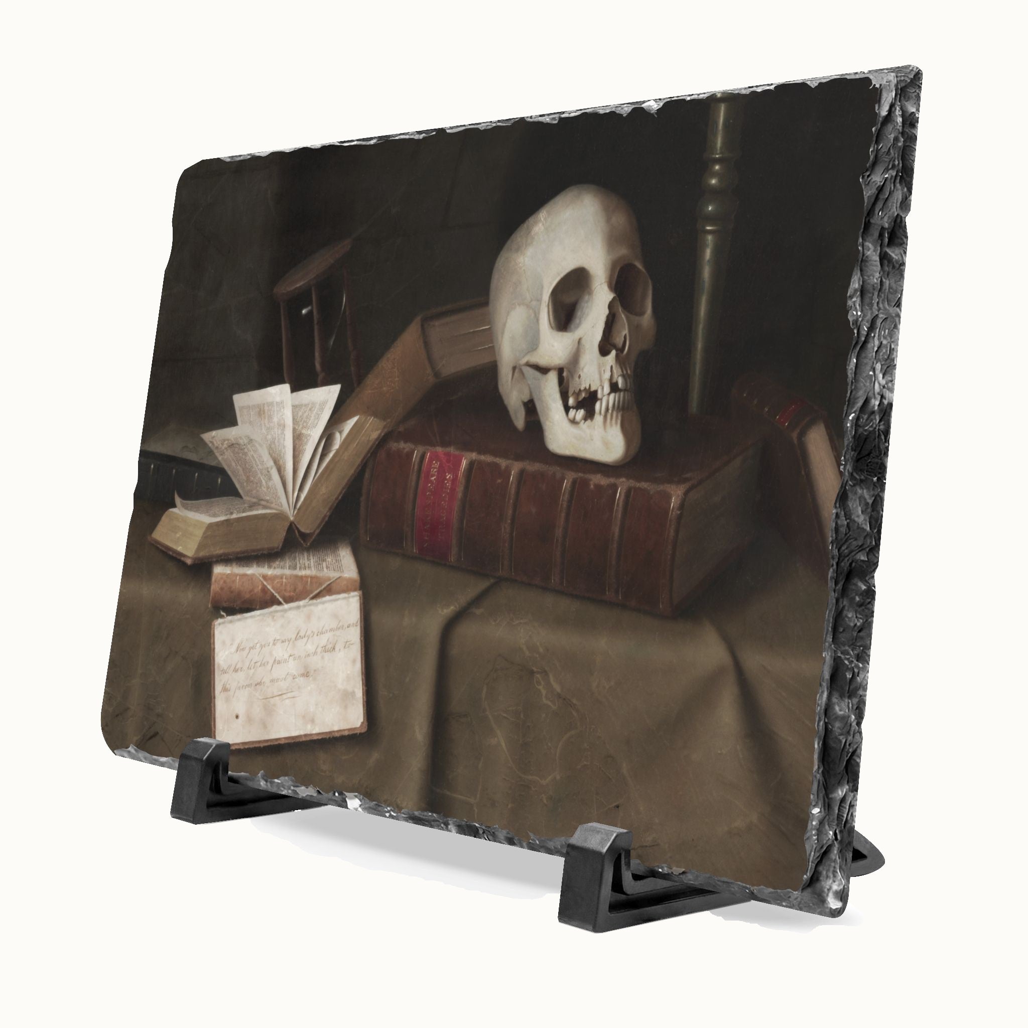 A rectangular slate plaque with a dark, moody still life print of a skull on old books, displayed on a black stand against a light gray background.