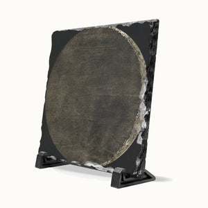 A square black stone plaque with a circular textured metallic center, displayed on a small black stand against a clean white background.