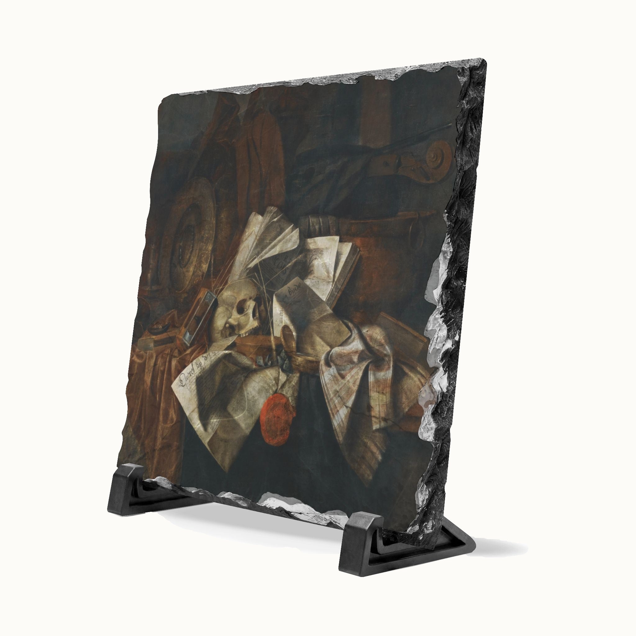 A rectangular black slate art plaque displaying a still life painting with a skull, draped fabric, and a small red apple, shown on a black display stand against a white background.