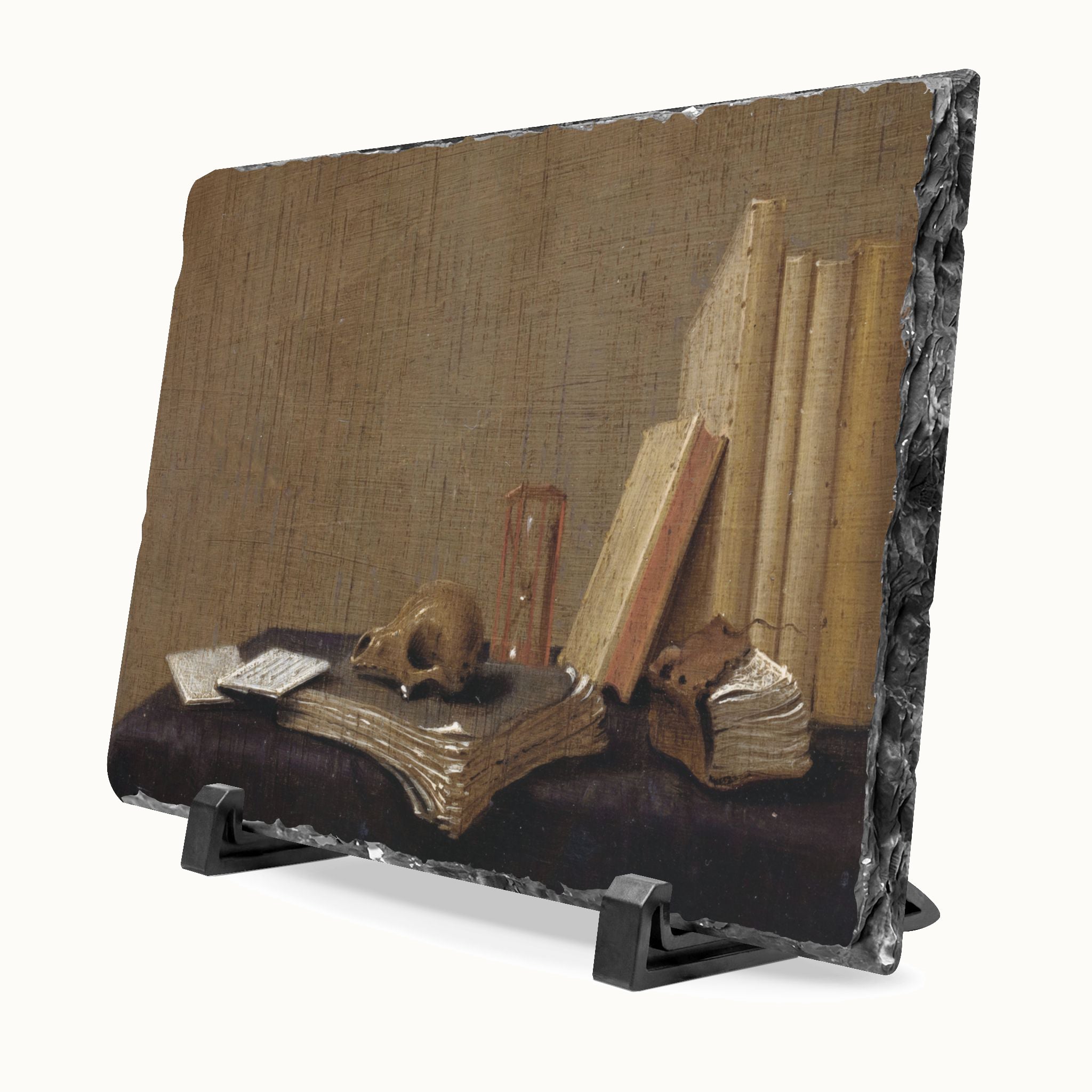 A rectangular decorative plaque or print with a still life artwork showing old books, a skull, and a small object on a dark surface, displayed on a black stand against a light gray background.