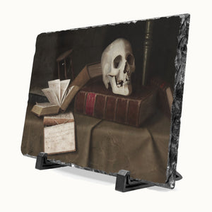 A rectangular slate plaque with a dark, moody still life print of a skull on old books, displayed on a black stand against a light gray background.
