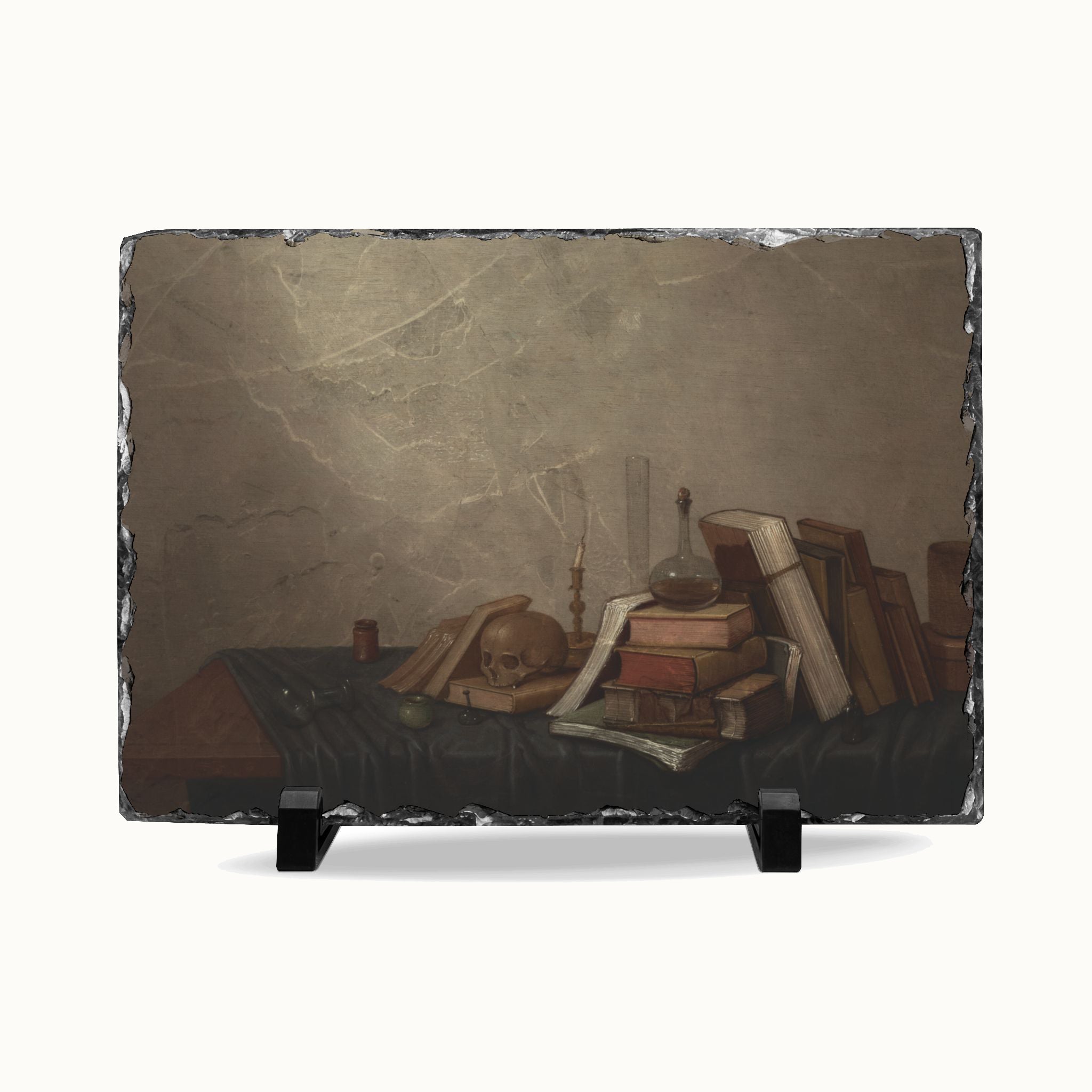 A rectangular slate serving board with a printed still life artwork of old books, a skull, candles, and a glass vessel on a dark table, displayed on a white background with two small black stands.