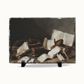 A rectangular slate art print featuring a classical still life painting of scattered old books and papers, displayed on a small black stand against a light gray background.