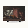 A rectangular slate serving board with a rustic dark gray stone edge, featuring a printed still life artwork of a brown pipe, a newspaper, and a terracotta jar. The board is displayed on two small black stands against a clean white background.