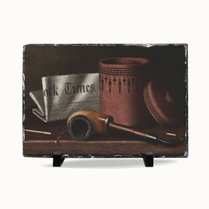 A rectangular slate serving board with a rustic dark gray stone edge, featuring a printed still life artwork of a brown pipe, a newspaper, and a terracotta jar. The board is displayed on two small black stands against a clean white background.
