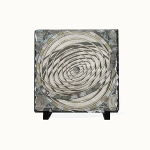 A square decorative tile or coaster featuring a spiral geometric pattern in cream, gray, and black, with a distressed money-print texture and small black display feet at the bottom, shown on a plain light background.