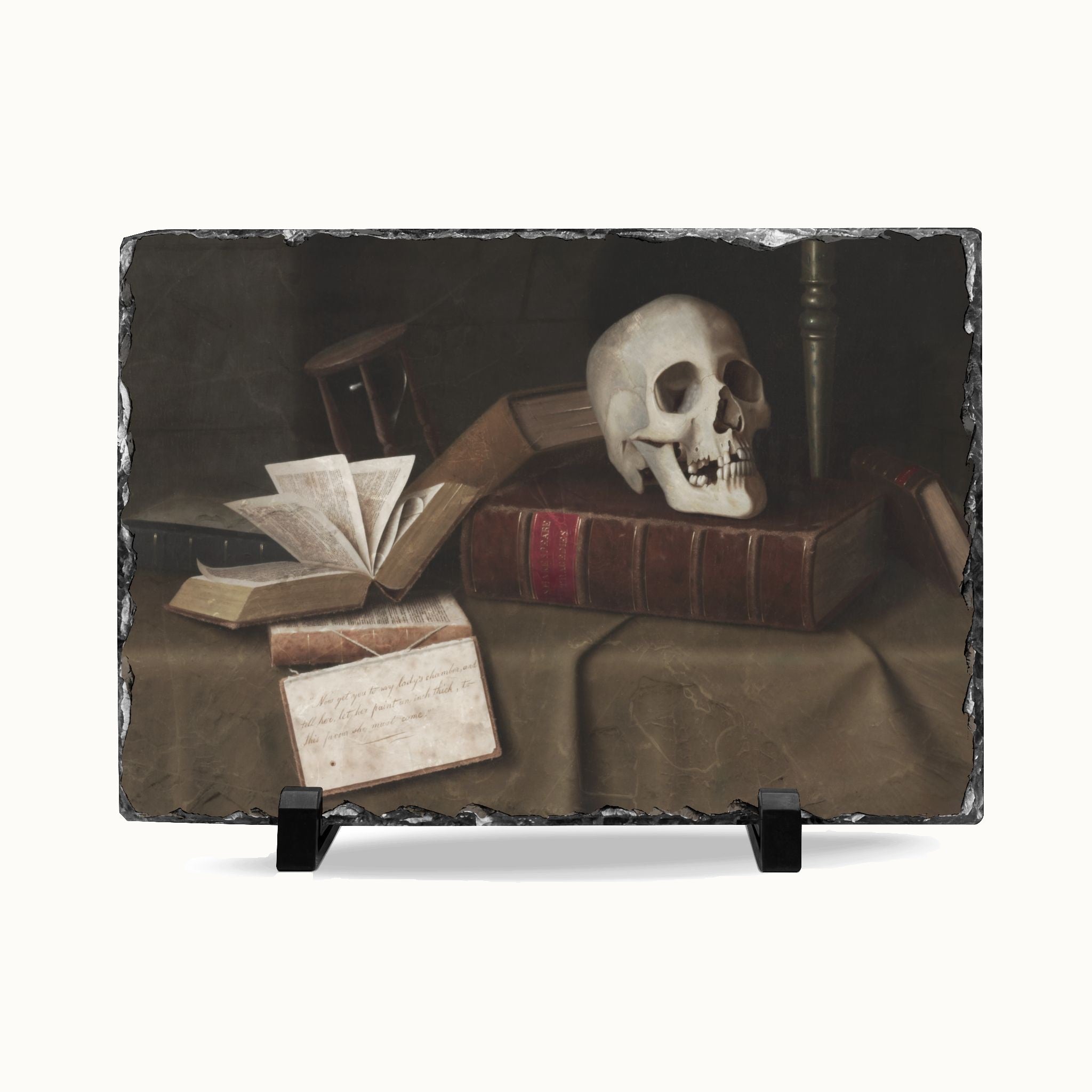 A rectangular slate sign featuring a classic still life painting of an open book, a skull resting on old books, and a handwritten note on a draped tablecloth, displayed on a black stand against a white background.