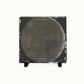 A square black slate art piece featuring a large circular design in textured gray and brown tones, displayed on a small black stand against a plain white background.