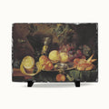 A rectangular slate serving board featuring a classic still life painting of fruit, displayed on a clean white background with two small black display stands.
