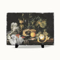 A rectangular slate serving board with a rustic dark gray edge, featuring a printed still life painting of grapes, fruit, cheese, and silverware. The board is displayed on two small black stands against a clean white background.
