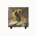 A square slate decorative tile featuring a still life painting of grapes, a lemon, and a bowl, displayed on a small black stand against a light gray background.