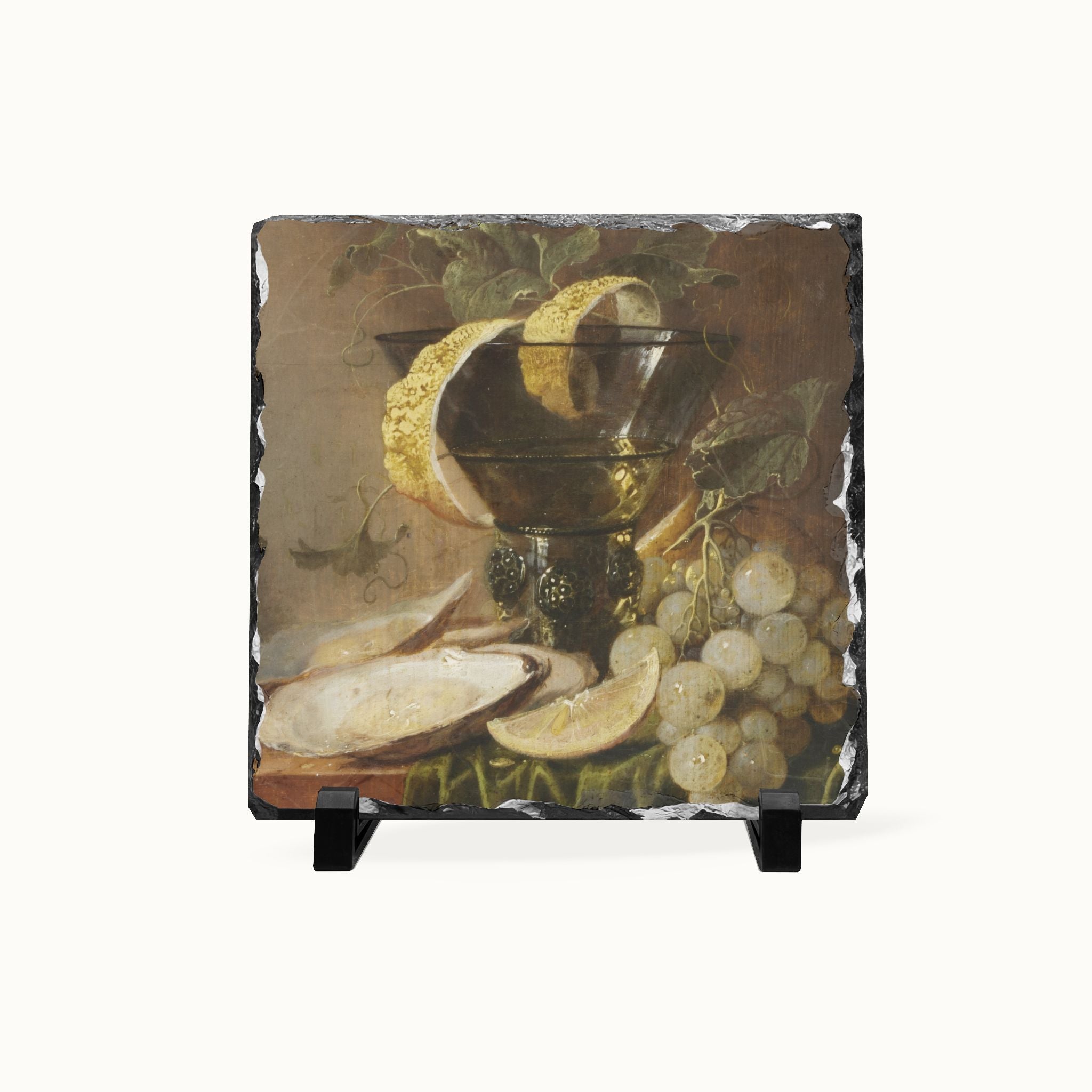 A square slate decorative tile featuring a still life painting of grapes, a lemon, and a bowl, displayed on a small black stand against a light gray background.